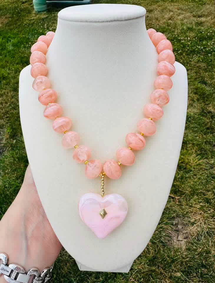 Pink marbled bead necklace with a pale pink heart pendant on a cream bust.
