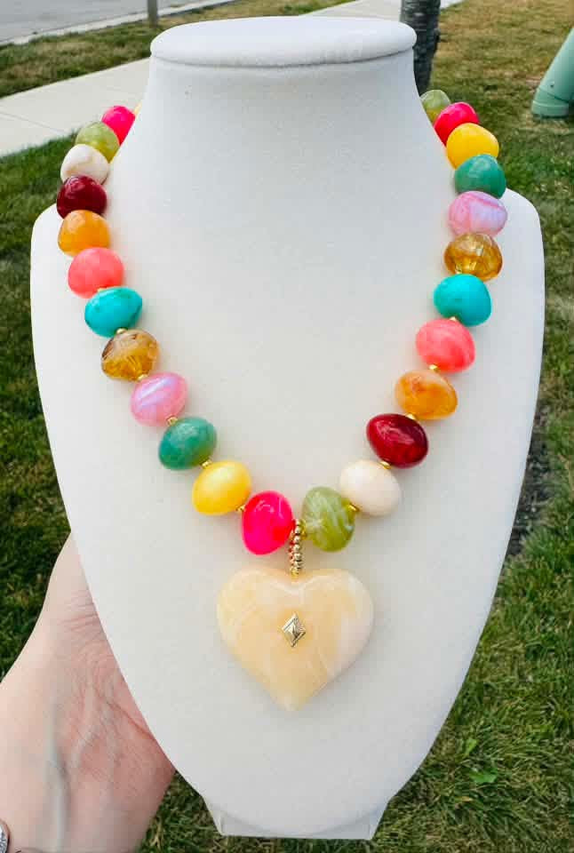 Multicolored beaded necklace with a cream heart pendant on a tabletop bust.