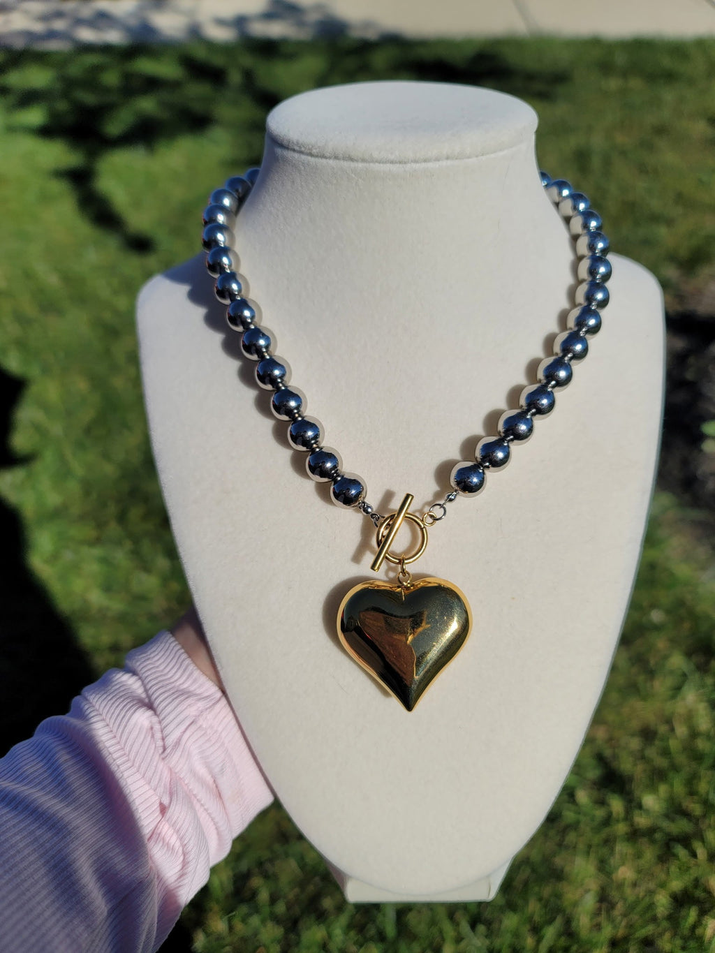 Silver-tone beaded necklace with a large gold-tone heart and front toggle clasp.