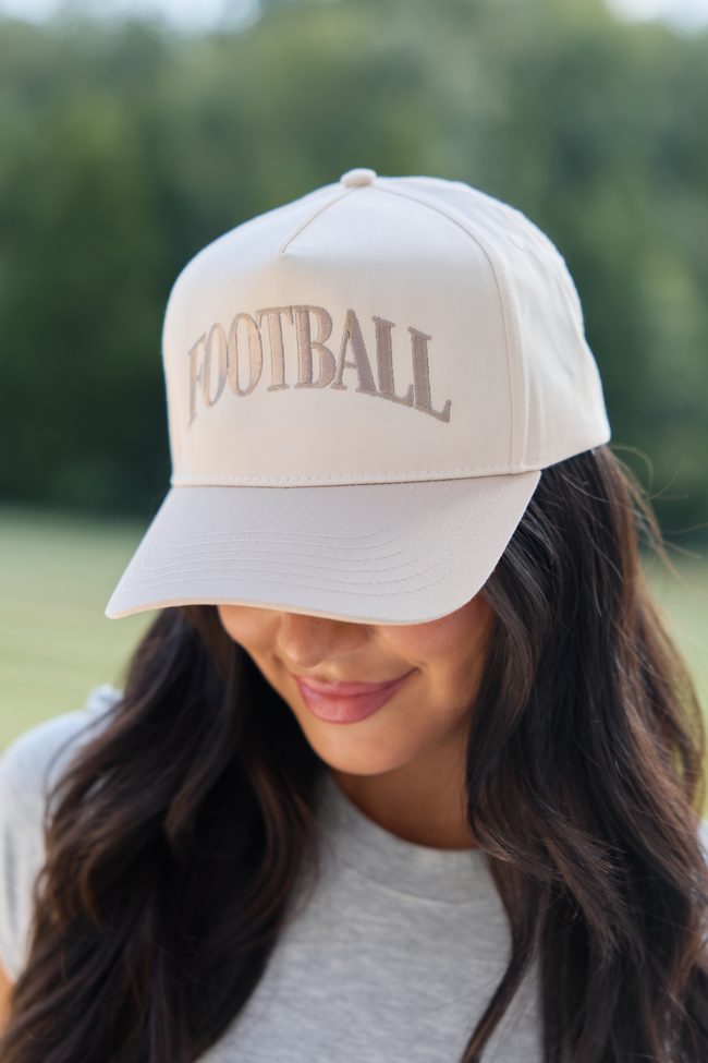 Natural hat with khaki FOOTBALL embroidery, worn with a gray top.