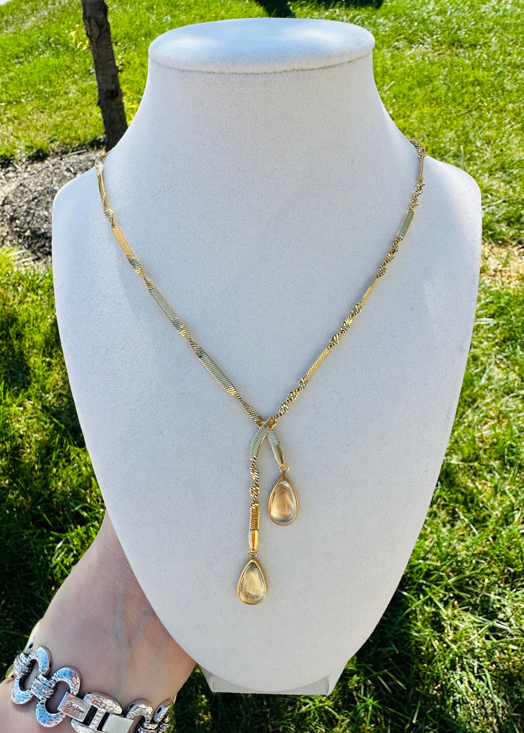 Gold-tone crossover necklace with two hanging teardrops on a cream bust.