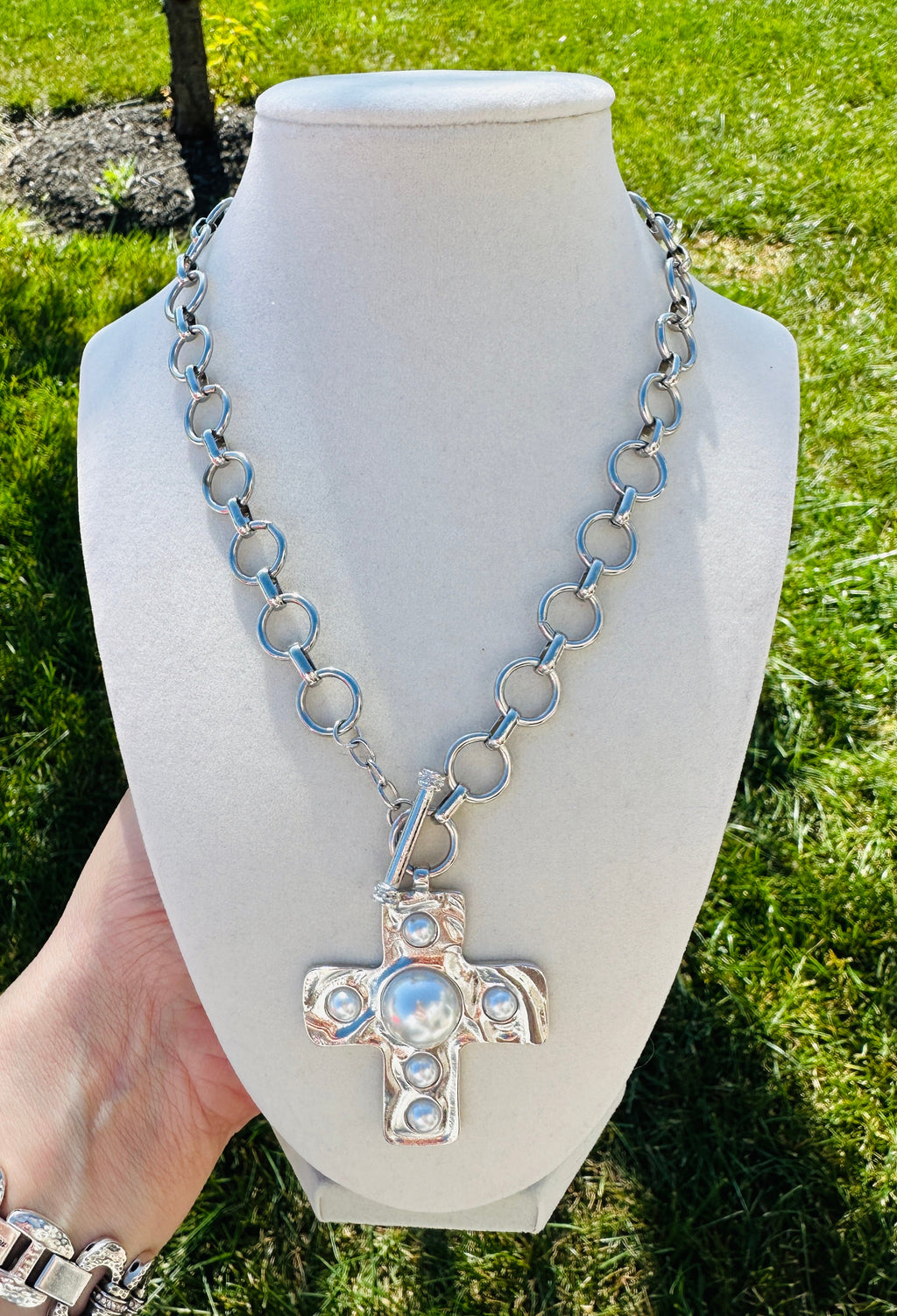 Silver-tone circular-link necklace with a faux-pearl cross pendant on a cream bust.