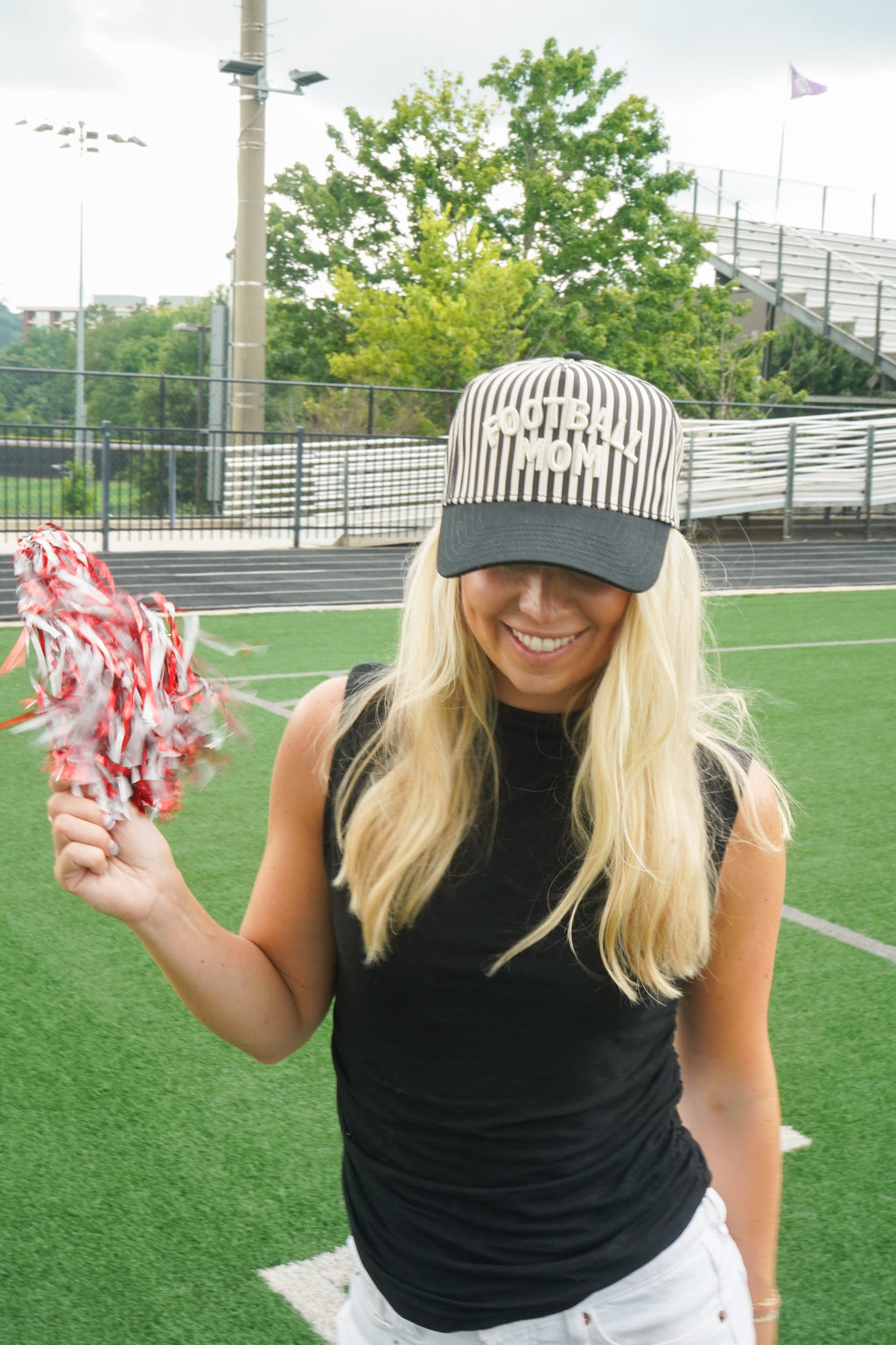 Close-up of a woman wearing a black and cream striped Football Mom hat with white raised lettering and a black bill.