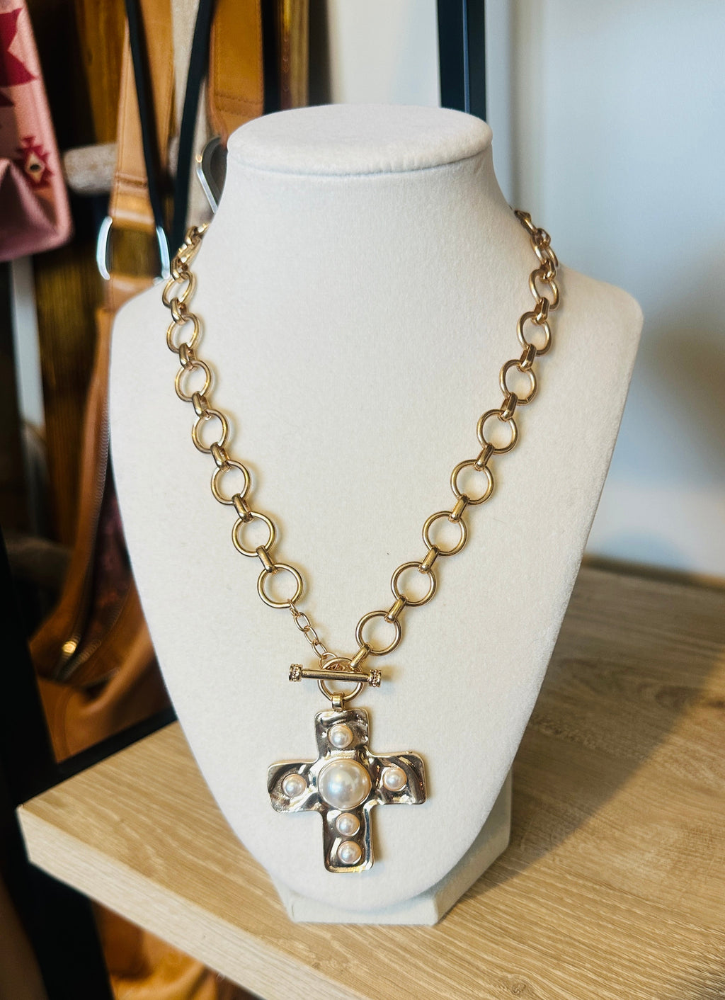 Gold-tone circular-link necklace with a faux-pearl cross pendant on a cream bust.
