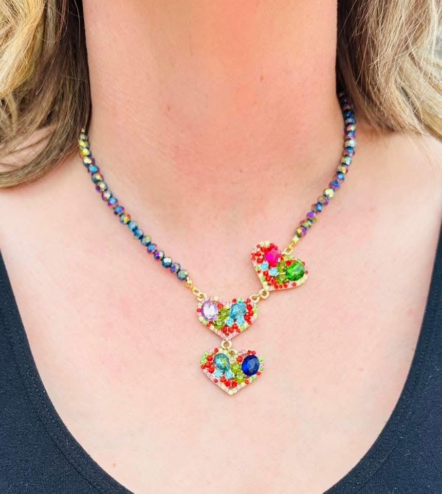 Multicolored bead necklace with three rainbow crystal hearts on a cream bust.