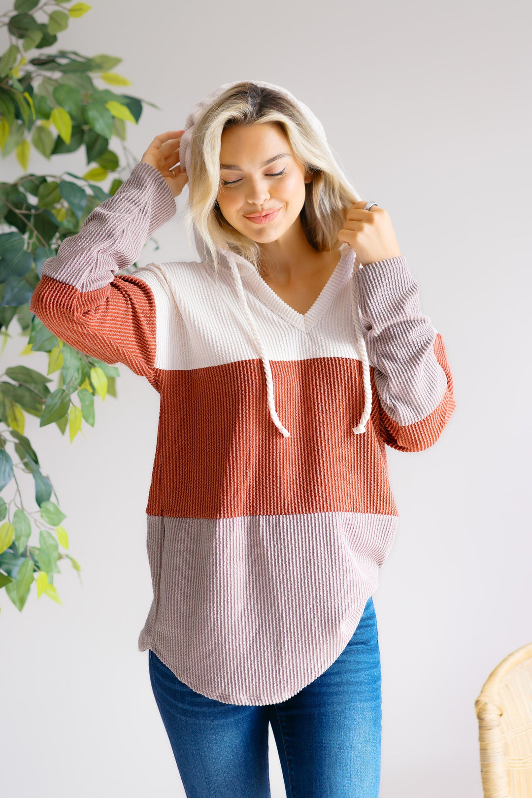 Model holding the hood of a cream, rust and mauve color-block pullover