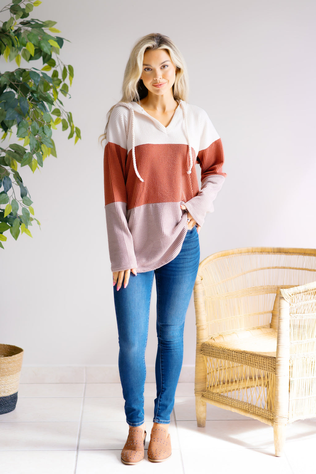 Model holding the hood of a cream, rust and mauve color-block pullover