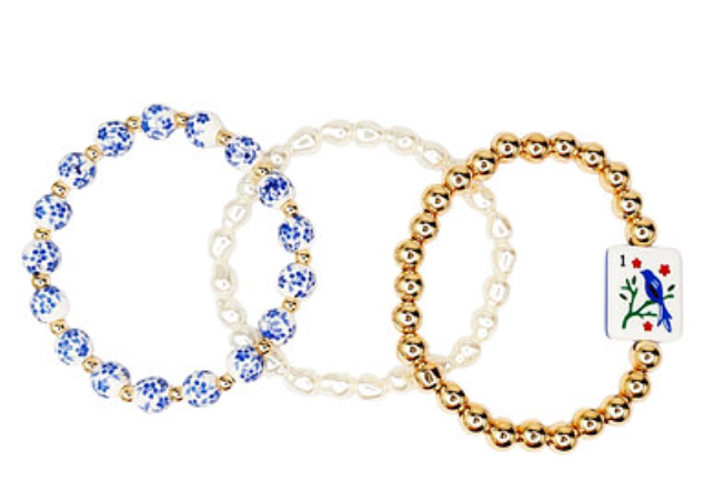 Stack of three Bird Bam bracelets with blue floral beads, faux pearls, and gold-tone beads with a bird tile charm.