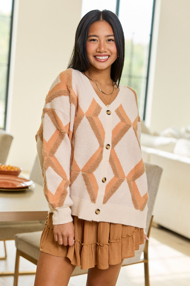 Seated front view with tan tiered skirt — cream button cardigan with peach and tan geometric diamonds.