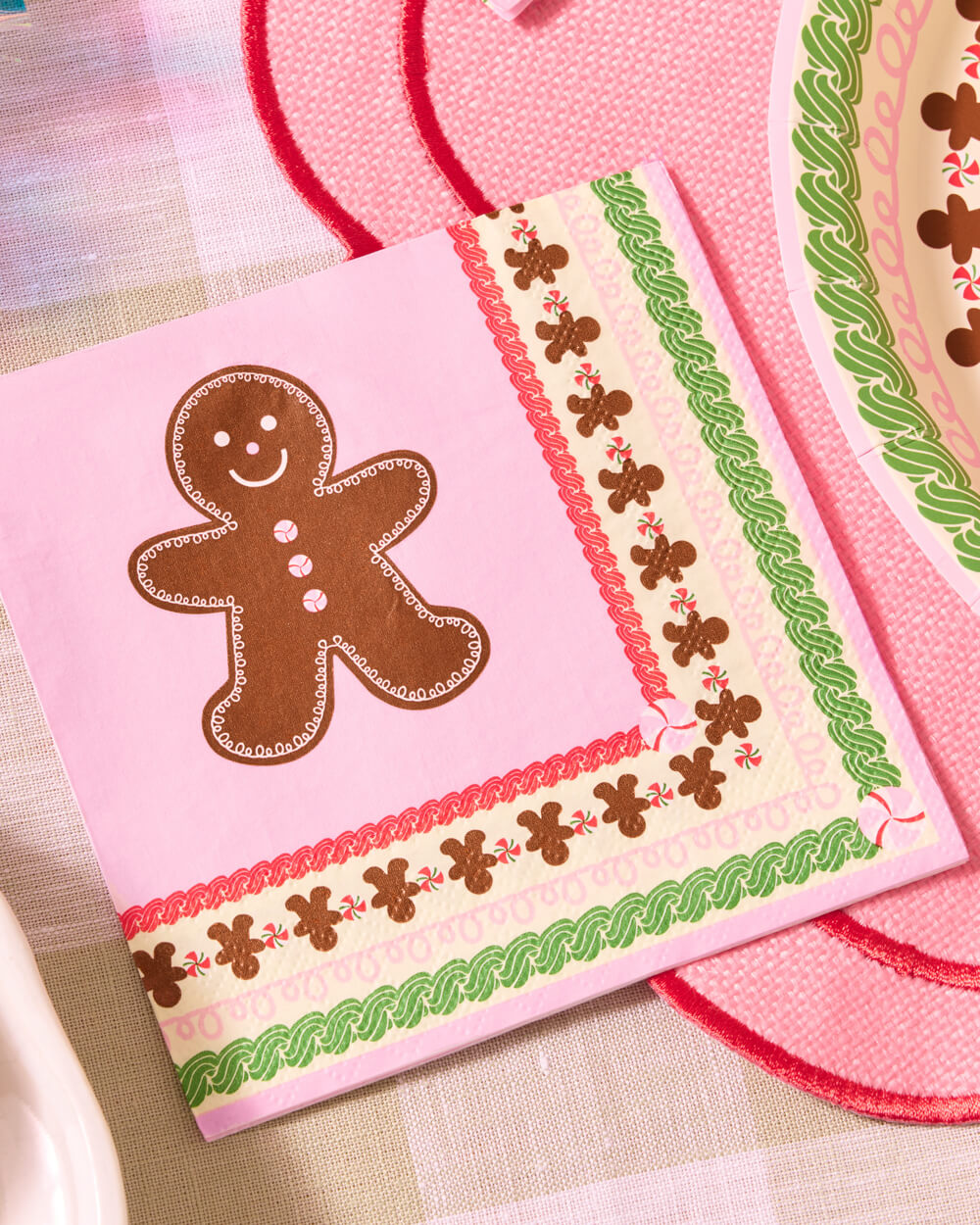 Pink gingerbread napkins with red and green borders on a holiday table.