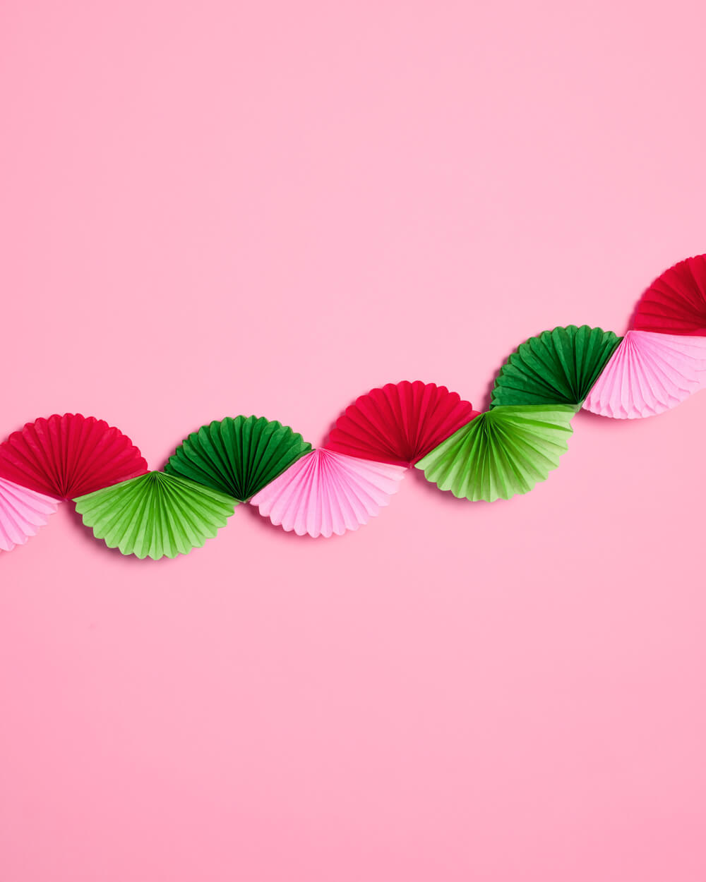 Red, pink, light green and dark green tissue fans forming a Christmas garland on pink.