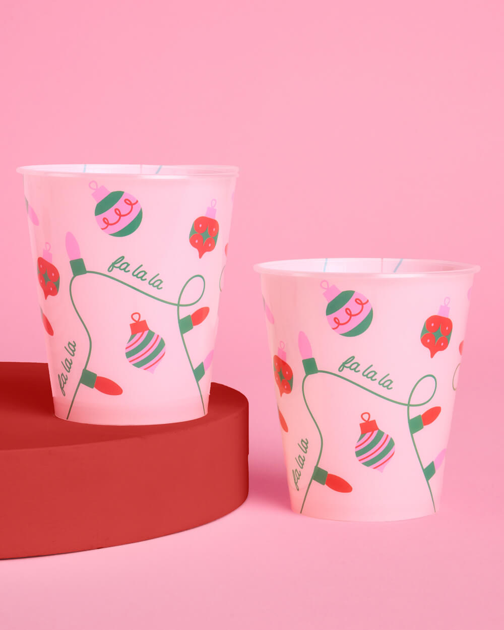Pink Merry Sipmas cups with ornaments and string lights on a festive table.